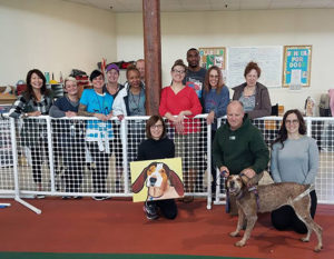 Hannah's adopters kneel with her in the Track and Training Center with staff and volunteers standing behind them