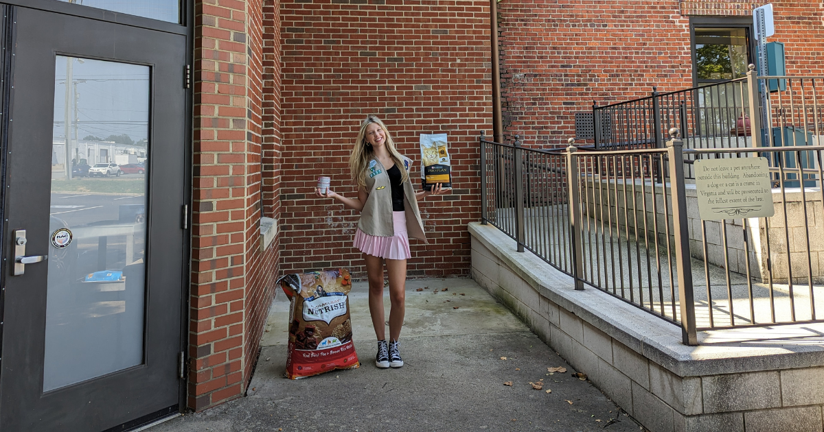 Teen standing on sidewalk in front of brick building holding pet food containers